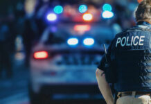 Ex Gov Hopeful Arrested On Drug Charges Police officer in a tactical vest standing in front of a police car with flashing lights