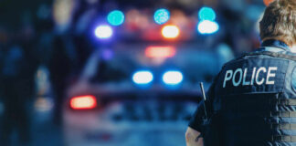Police officer in a tactical vest standing in front of a police car with flashing lights