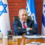 man in suit seated at desk with Israeli flags