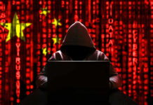 Declassified Files Detail Massive Voter Database A hooded figure sitting in front of a laptop with a red digital background