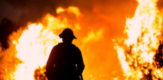 Silhouette of a firefighter standing in front of a large wildfire