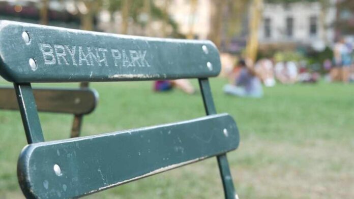 New,York,City,,Manhattan,Midtown,Bryant,Park,With,Public,Library, Green metal park chair with people relaxing on a lawn in the background