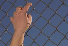 Spain’s Aid Numbers Spark Outrage Hand gripping a chain-link fence