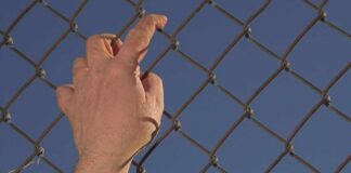Spain’s Aid Numbers Spark Outrage Hand gripping a chain-link fence