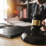 Judge's gavel on desk with person reading documents in background