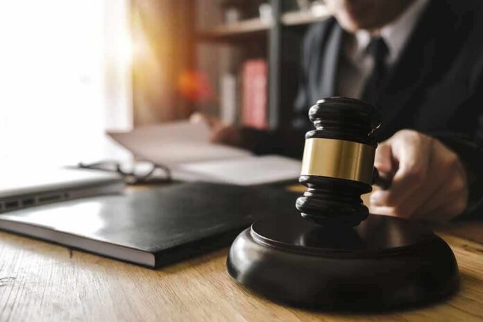 Judge's gavel on desk with person reading documents in background