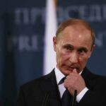 Shock Death Scrambles Russia Sanctions Push man in suit at podium touching his face