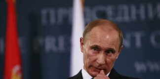 man in suit at podium touching his face