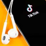 Policy Whiplash: TikTok Marches Back In Smartphone with TikTok app and white wired earbuds on yellow background
