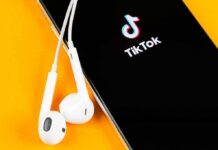 Smartphone with TikTok app and white wired earbuds on yellow background