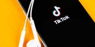 Policy Whiplash: TikTok Marches Back In Smartphone with TikTok app and white wired earbuds on yellow background