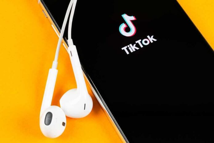 Smartphone with TikTok app and white wired earbuds on yellow background