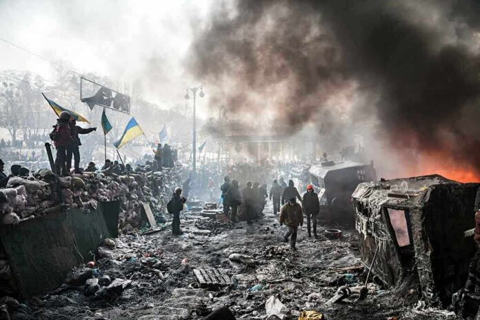 shutterstock_173329988 A chaotic protest scene with smoke, fire, and people holding flags