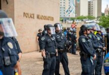 Police officers in riot gear stand in formation outside a headquarters building