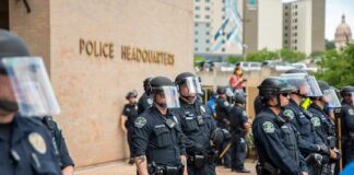 Police officers in riot gear stand in formation outside a headquarters building
