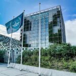 Modern glass office building with blue flag and greenery
