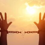 raised hands breaking chains against a sunset sky
