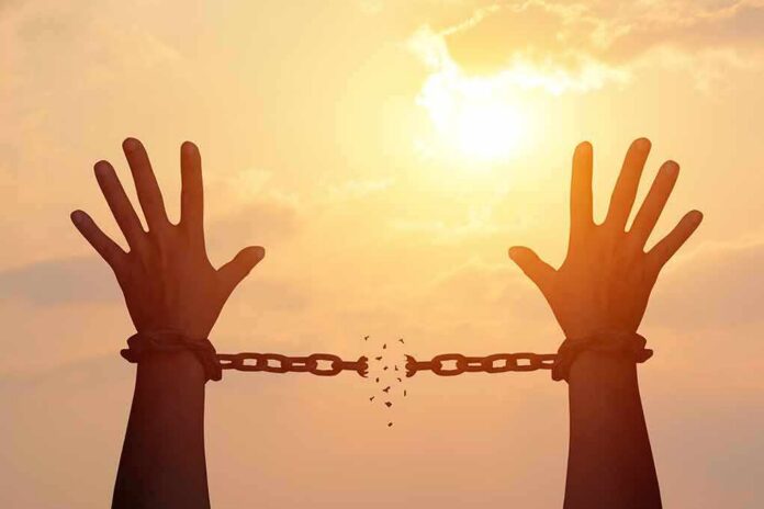 shutterstock_1049795408 raised hands breaking chains against a sunset sky