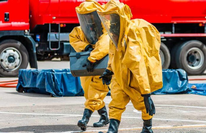 shutterstock_1110628994 Hazmat workers in yellow suits carry equipment near a tanker truck