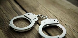 Police Tighten Net In Hanging Death Metal handcuffs on wooden surface