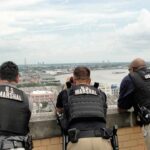 America’s Longest Medical Fugitive Caught Three U.S. Marshals in tactical vests overlooking a city and river