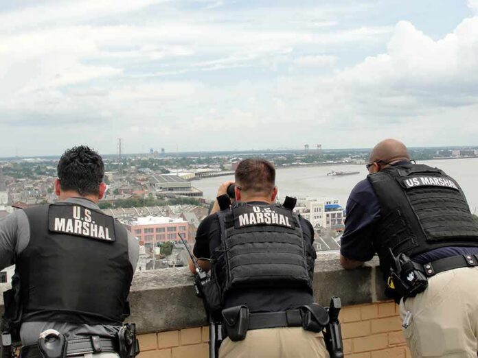 shutterstock_1473238355 Three U.S. Marshals in tactical vests overlooking a city and river