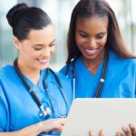 Mystery Parasite Sickens Americans Nationwide Two nurses in blue scrubs looking at a tablet