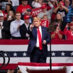 Heckler Clash Hijacks Trump Rally man in suit points from a stage at a political rally