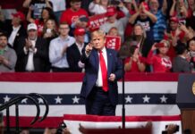 Heckler Clash Hijacks Trump Rally man in suit points from a stage at a political rally