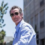 DOJ Subpoenas Rock Newsom’s Travel Tab man in sunglasses wearing a light blue shirt outdoors