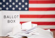 Mail-Vote Exemption Masks Risky Power Play Ballot box with papers in front of an American flag