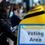 Costly VICTORY: $30M Smashes GOP Record voter wearing a mask using a yellow ballot box