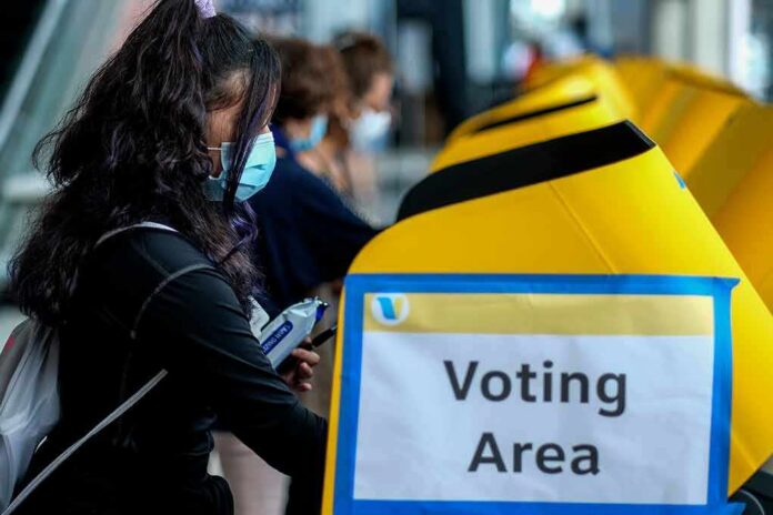 shutterstock_1840091617 voter wearing a mask using a yellow ballot box