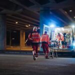 Paramedics load a stretcher into an ambulance at night under an overpass
