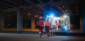 Paramedics load a stretcher into an ambulance at night under an overpass