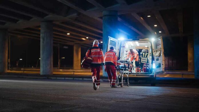 shutterstock_1878018094 Paramedics load a stretcher into an ambulance at night under an overpass