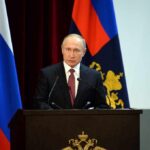 speaker at podium with flags in background