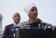 Woman in white headwrap speaking at microphones outdoors