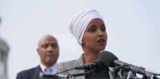Marriage Fraud Bombshell Shadows Ilhan Omar Woman in white headwrap speaking at microphones outdoors