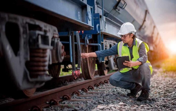 Railway inspector checking freight train wheel with tablet