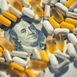 Medicare For All – With A Catch pills and capsules scattered over a hundred-dollar bill