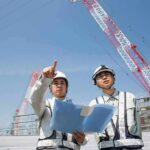 Court Clash Over Trump’s Underground Build Two construction workers reviewing plans at a site with cranes