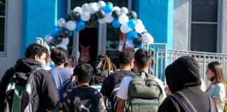 Students with backpacks enter a school under a balloon arch