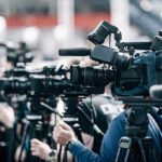 Parents Sue After FBI Red Flag Snubbed Broadcast cameras on tripods at a press event
