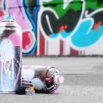 spray paint cans on pavement in front of a graffiti wall