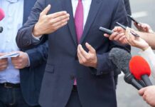 Hypocrisy Bomb Explodes in Harrisburg Businessperson in suit speaking to reporters with microphones