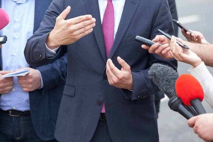 Businessperson in suit speaking to reporters with microphones