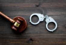 Judge's gavel and metal handcuffs on wooden table