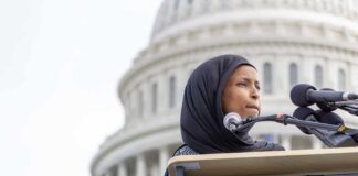 Ilhan Omar speaking at a podium with microphones in front of the U.S. Capitol