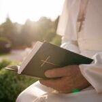 New Report Exposes Decades Of Abuse Person in white robe holding a Bible outdoors